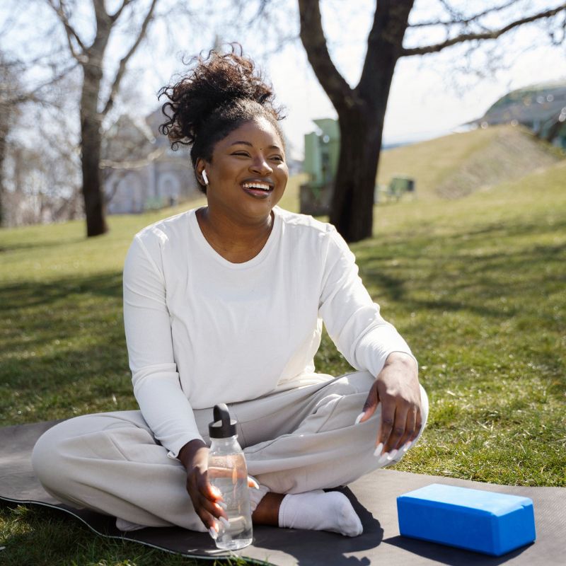 Black woman sitting on mat in park with water bottle