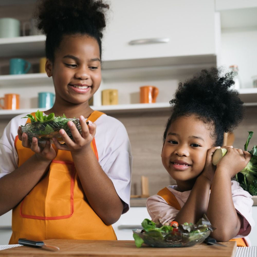 Two Black girls eating vegetables in a kitchen
